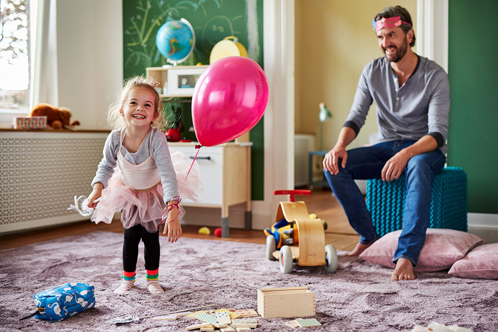 A photo of a father playing with his daughter while she is holding a balloon and wearing a ballerina dress